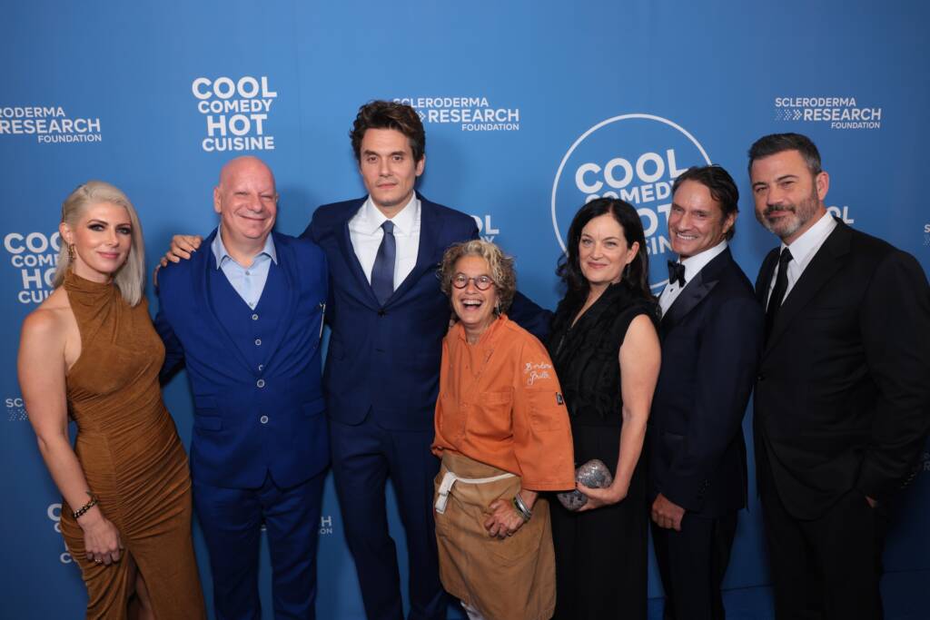 A group of people posing at the Cool Comedy Hot Cuisine event by the Scleroderma Research Foundation, standing in front of a blue backdrop with the event's name and foundation logo.